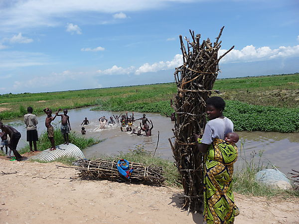 Woman With Baby And Huge Firewood And Children Enjoying The River